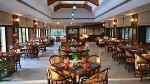 Un vaste espace dédié à la salle à manger, doté de hauts plafonds et de poutres en bois, comprenant plusieurs tables et des chaises en osier.