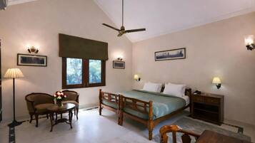 A bedroom with a bed, a chair, a table, a standing lamp, and a ceiling fan.