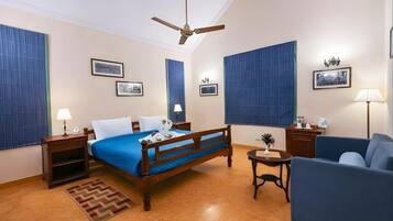 A hotel room with a bed, a desk, a chair, a ceiling fan, and a small table with a plant.