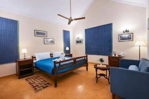 A hotel room with a bed, a desk, a chair, a ceiling fan, and a small table with a plant. - Justa The Bagh, Kanha (Baihar)