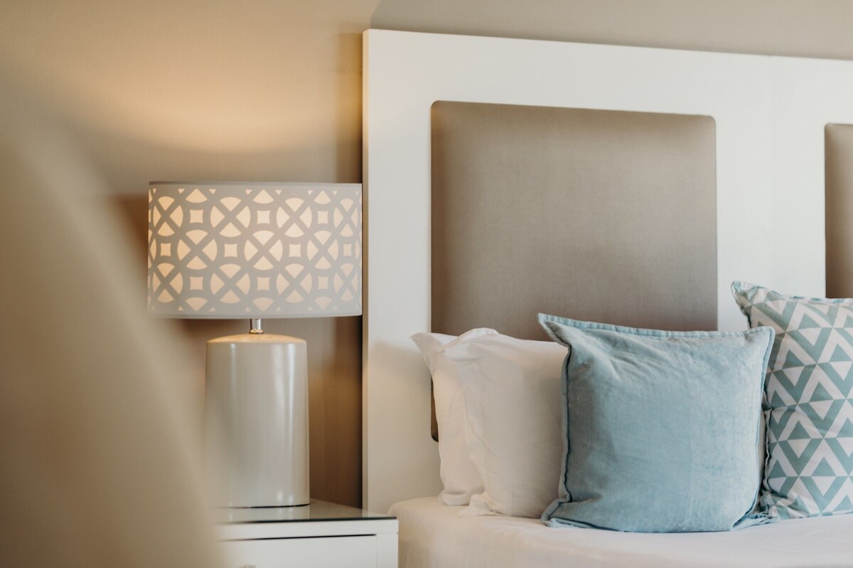 A neatly made bed with a headboard, a bedside lamp with a geometric pattern, and two pillows with a geometric design.