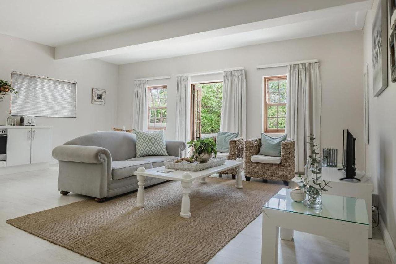 A living room with a sofa, a coffee table, and a wicker chair. There are windows with curtains, a fireplace, and a framed picture on the wall.
