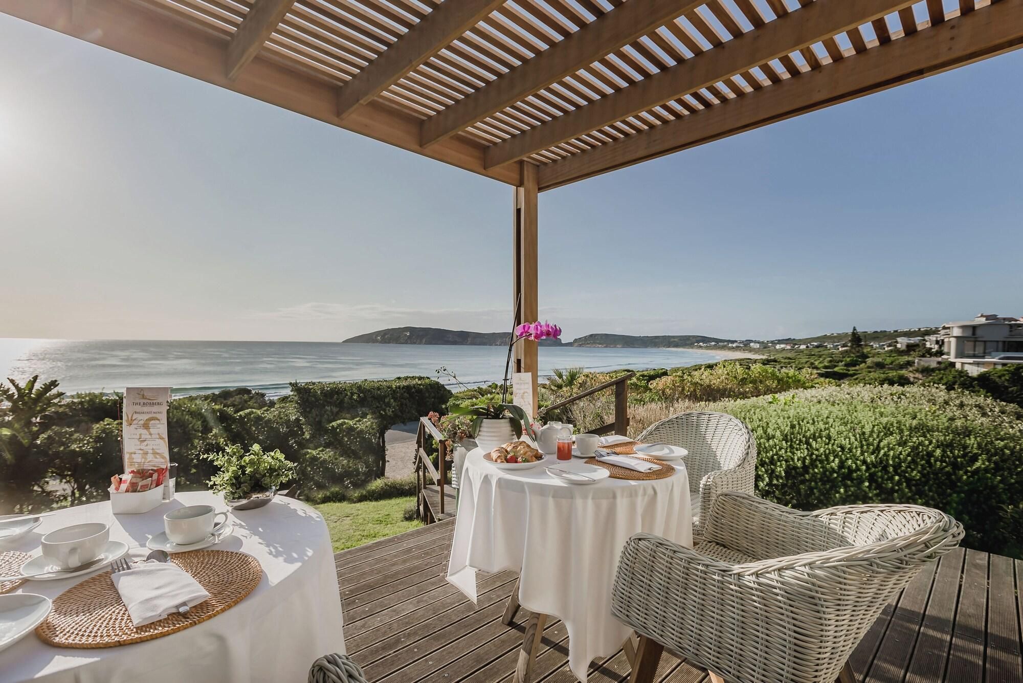 A seaside dining area with tables set for two, overlooking the ocean.