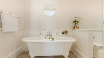 A bathroom with a freestanding bathtub, a toilet, a mirror, and a shelf with decorative items.