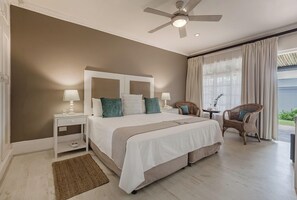 A bedroom with a bed, nightstands, a ceiling fan, a window with curtains, and wicker chairs. - Cottage Pie Guest House (Plettenberg Bay)