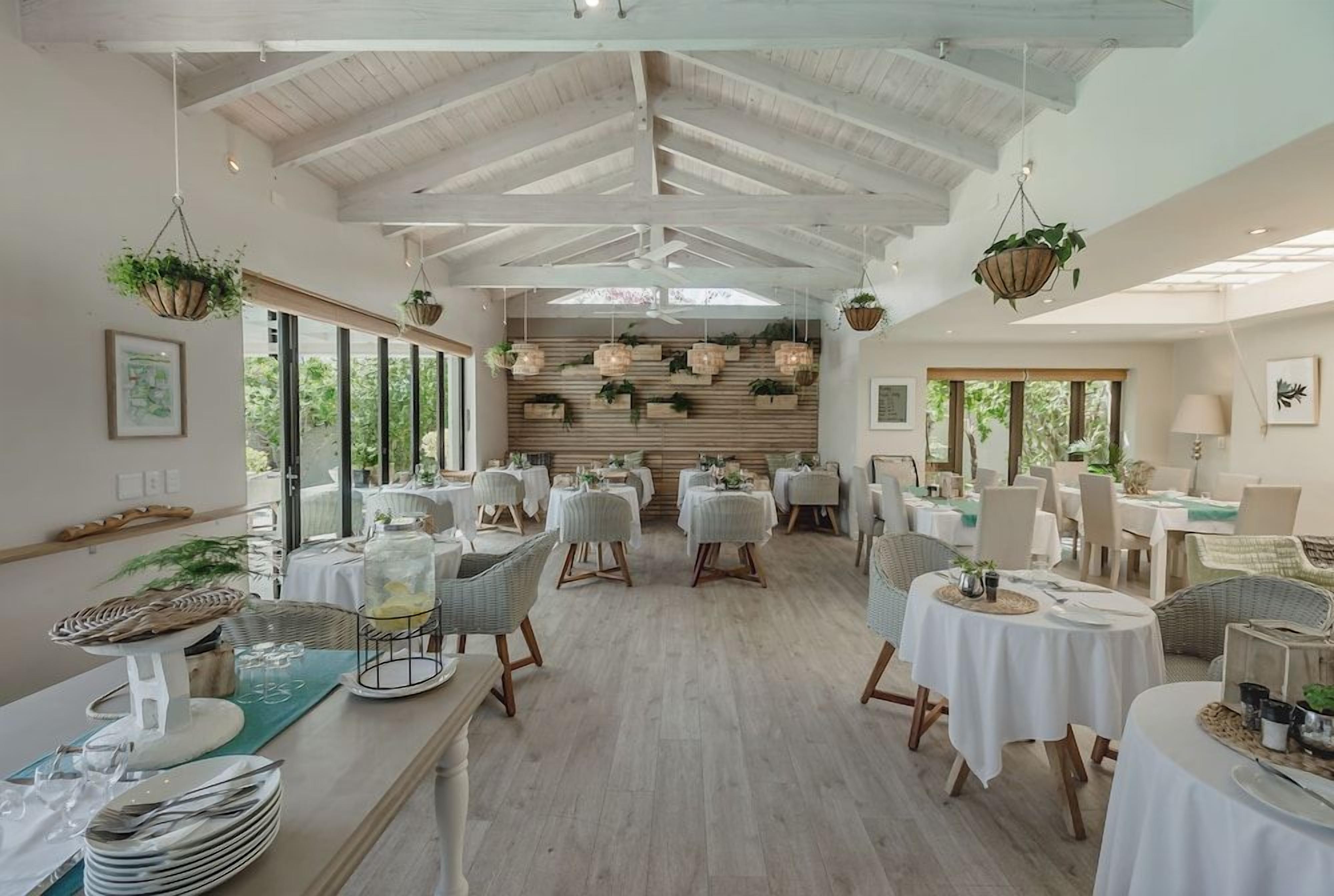 Zona de menjador àmplia amb sostres alts, diverses taules preparades per dinar i plantes penjants.