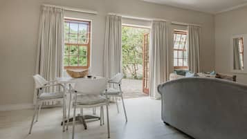 A room with a dining table, chairs, a sofa, and a view of a garden through open doors.