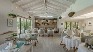 Un comedor espacioso con techos altos y plantas colgantes, con mesas dispuestas para comer y sillas alrededor.