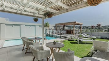 Una terraza en la azotea con piscina, sillones de descanso y un área de estar cubierta.