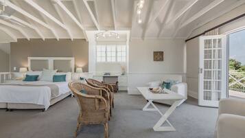 A spacious bedroom with a large bed, a desk, wicker chairs, and a balcony with a view.