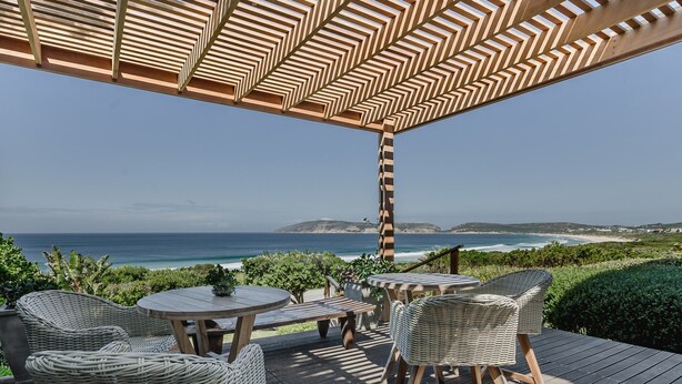 Un patio al aire libre con mobiliario de mimbre, una mesa de madera y vistas al océano.