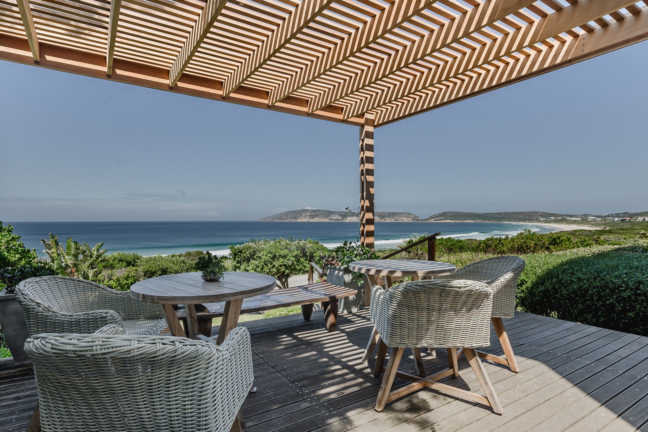 Un patio al aire libre con mobiliario de mimbre, una mesa de madera y vistas al océano.