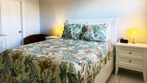 Un dormitorio con una cama, dos mesitas de noche, una silla y una puerta.