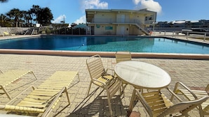 Una piscina con sillas de descanso y una mesa, rodeada por un edificio con balcón.