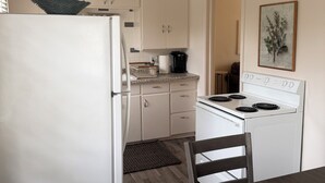 Keittiössä on valkoiset kaapit, jääkaappi, liesi ja ruokapöytä tuoleineen.
