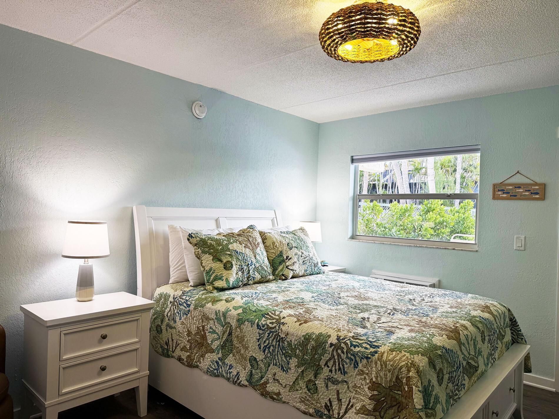 Une chambre à coucher comprenant un lit, des tables de chevet, une fenêtre avec vue et un luminaire au plafond.