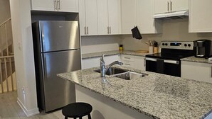 Una cocina moderna con armarios blancos, un refrigerador de acero inoxidable, una encimera de granito y dos taburetes negros.