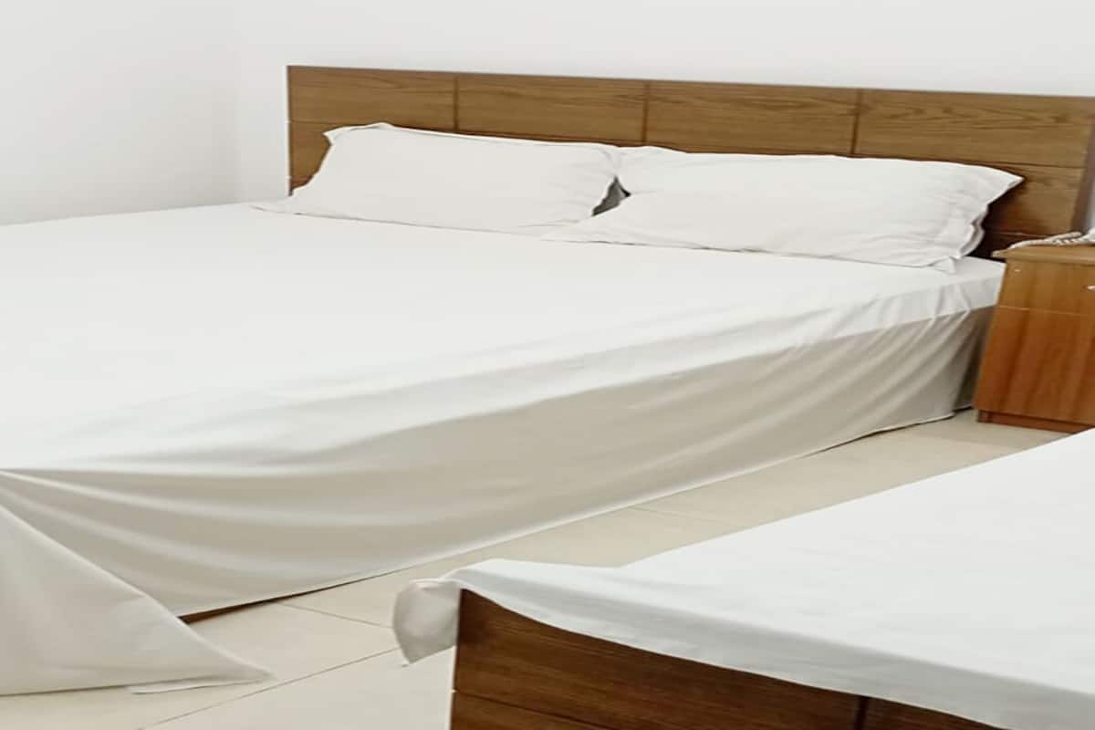 A neatly made bed with white linens, a wooden headboard, and a wooden nightstand beside it.