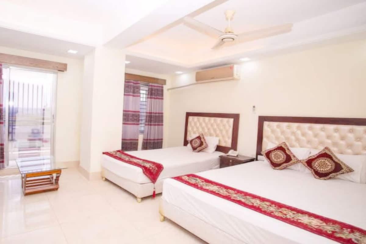 A hotel room with two beds, a sofa, a ceiling fan, and a large window with curtains.