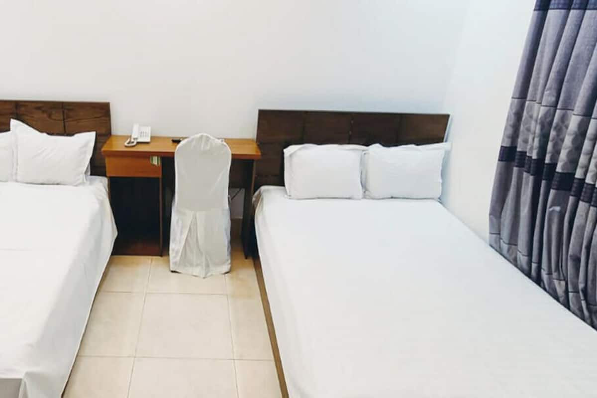 A hotel room with two single beds, a wooden desk with a telephone, and a chair.