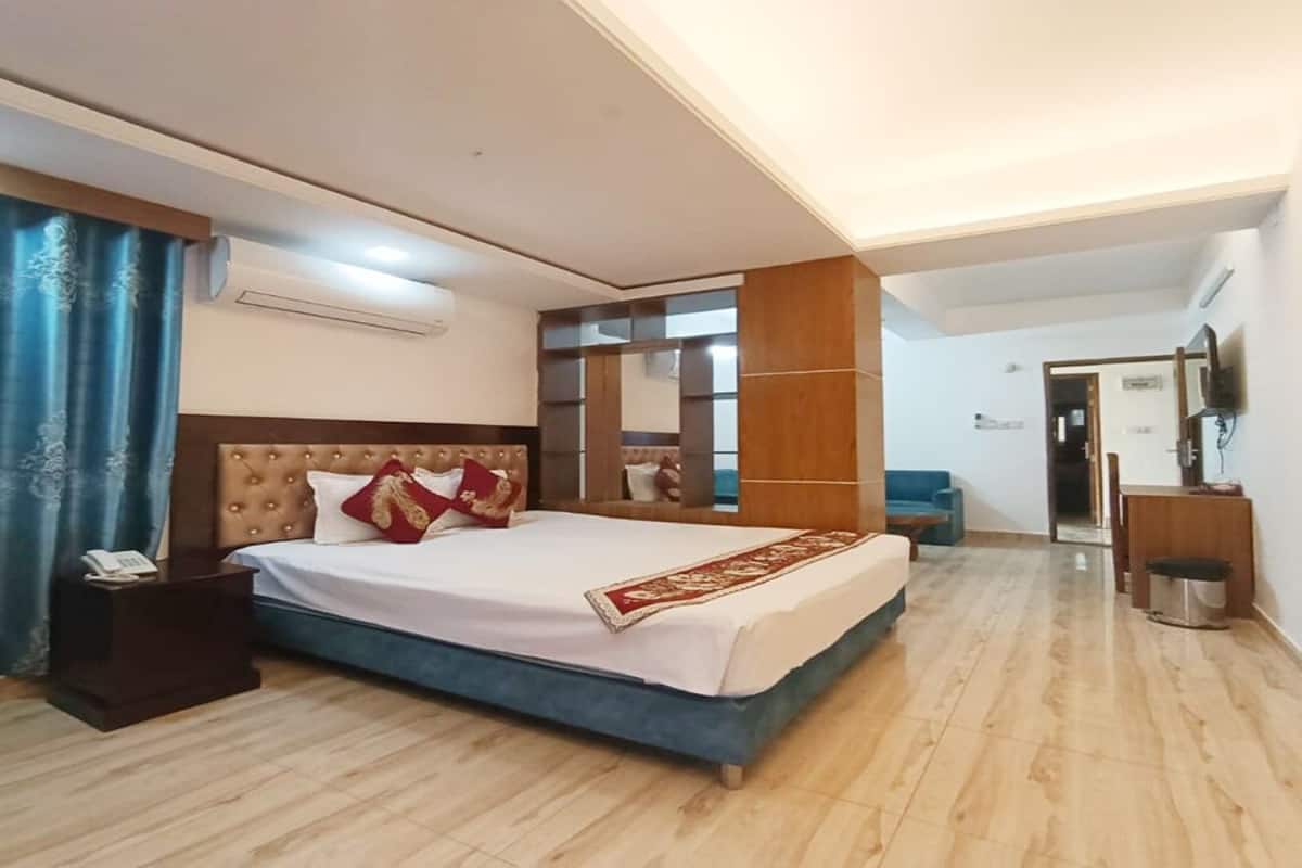 A hotel room with a large bed, a bedside table, a mirror, a TV, and a blue curtain.