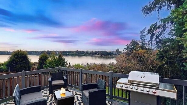 Eine Terrasse mit Gartenmöbeln und Grill, mit Blick auf einen See.