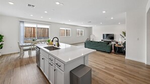 A modern kitchen with a central island, a dining area with a table and chairs, and a living area with a sofa and TV. - Sleeps ~12, 5 Bedroom 3 Bath Home in Lincoln CA (Lincoln)