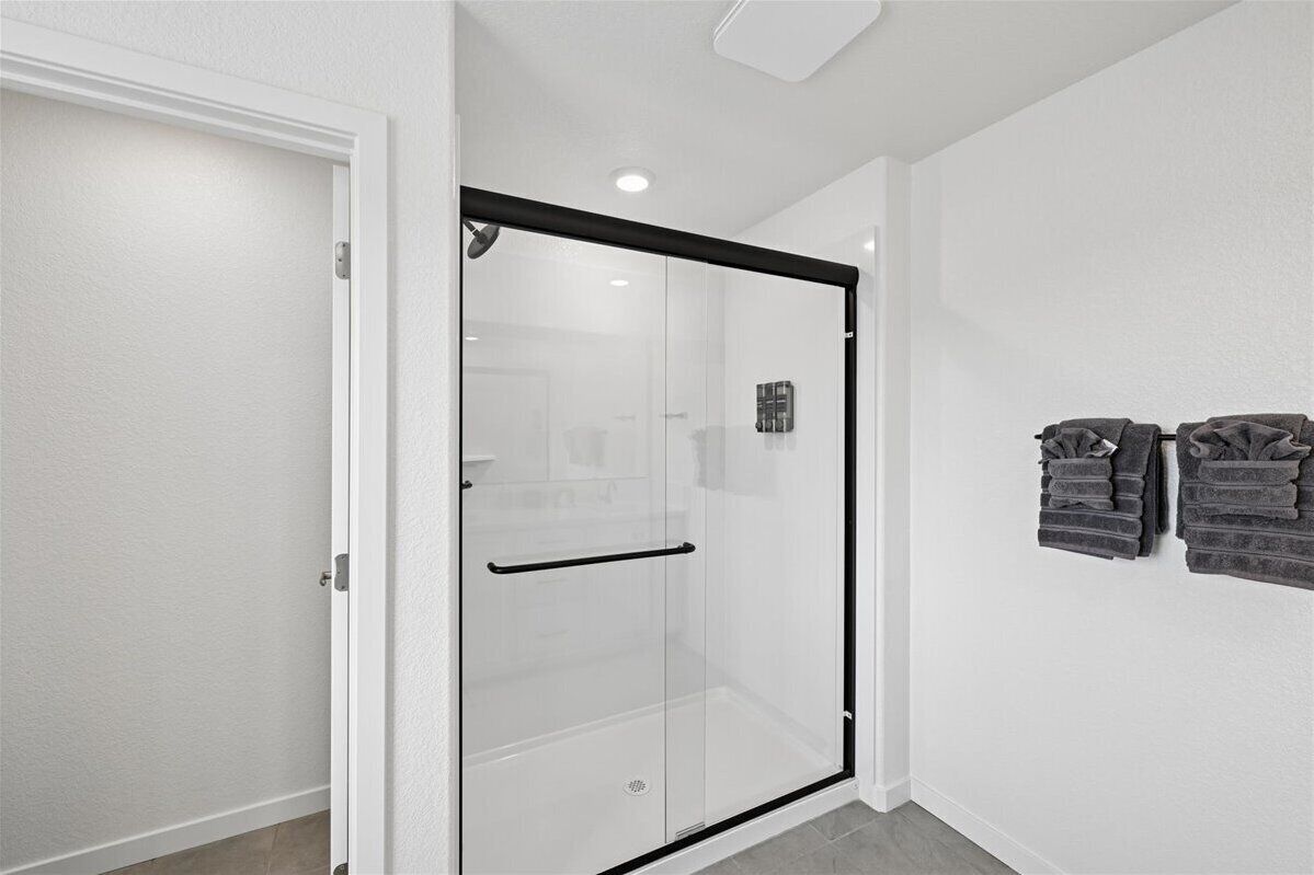 Una cabina doccia con pareti in vetro, cornice nera, porta bianca e un portascopevoli con asciugamani piegati a parete.