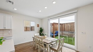 A dining area with a table and chairs, a window with blinds, and a view of a backyard with a wooden fence and a blue chair. - Sleeps ~12, 5 Bedroom 3 Bath Home in Lincoln CA (Lincoln)