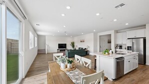 A modern kitchen with white cabinets, a stainless steel refrigerator, and a dining area with a wooden table and chairs. - Sleeps ~12, 5 Bedroom 3 Bath Home in Lincoln CA (Lincoln)