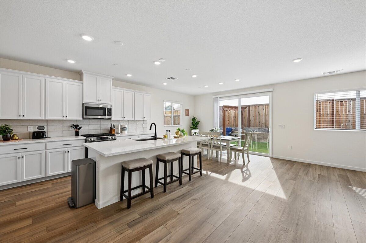 A modern kitchen with white cabinets, a central island with stools, a microwave, and a large window overlooking a wooden deck.