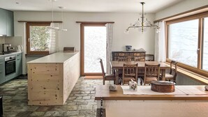 Eine moderne Küche mit Kochinsel, einem Essbereich mit Holzkästen und großen Fenstern mit Blick ins Freie.