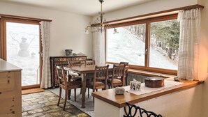 Ein Essbereich mit Holztisch und Stühlen, einer Kristallleuchtre und Blick auf eine verschneite Landschaft durch große Fenster.