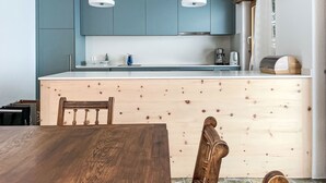 Eine moderne Küche mit Holzschränken, einer zentralen Kochinsel, Pendelleuchten und einem Essbereich mit Holztisch und Stühlen.