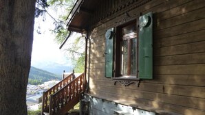 A wooden cabin with a wooden staircase and a window with green shutters.