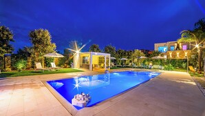 Uma piscina com cobertura de vidro, rodeada por espreguiçadeiras e guarda-sóis, e um terraço bem iluminado.