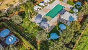 Vista aérea de uma propriedade residencial com piscina, espreguiçadeiras e um espaço coberto de varanda.