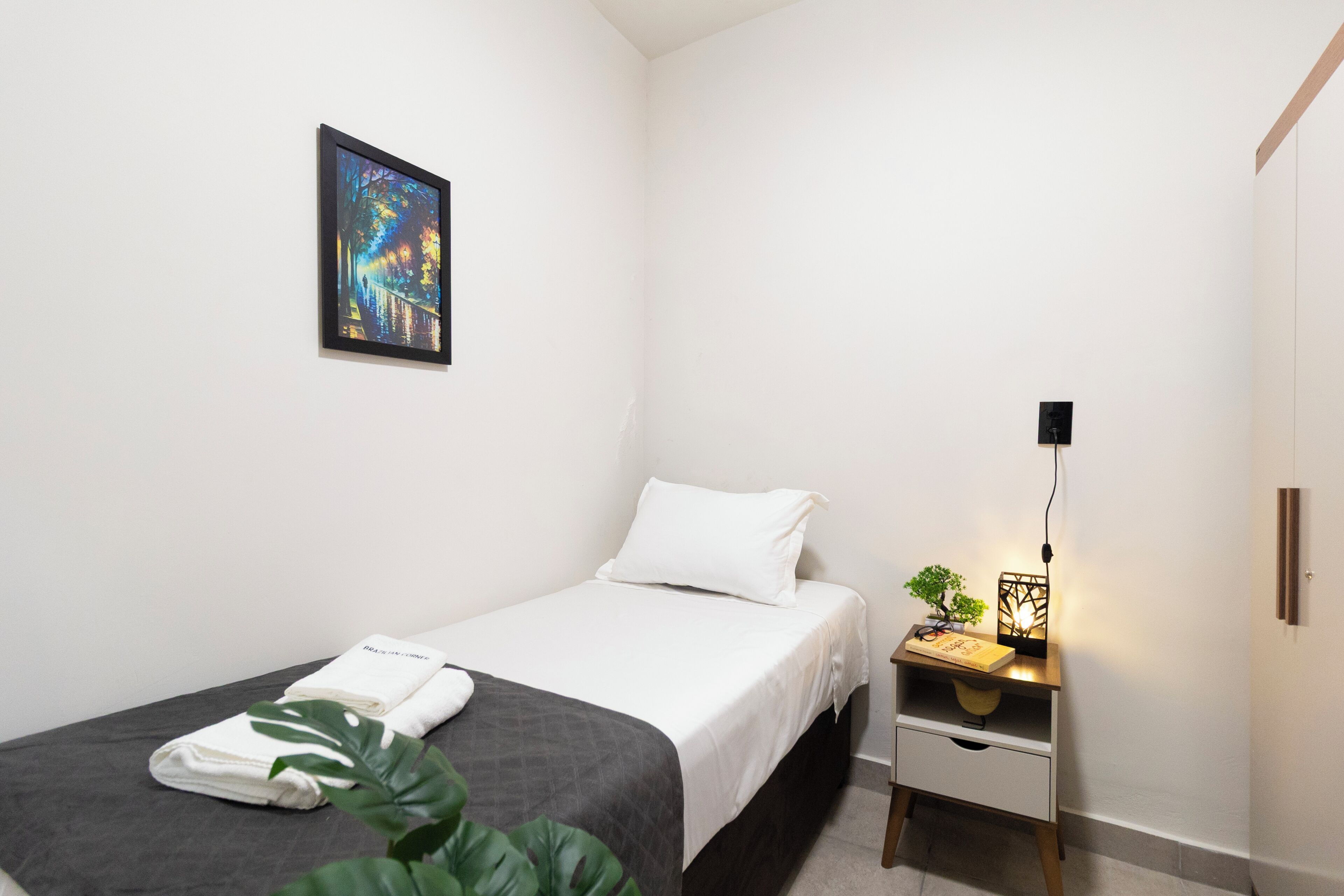 A small, neatly arranged bedroom with a bed, bedside table, and a wall-mounted picture.