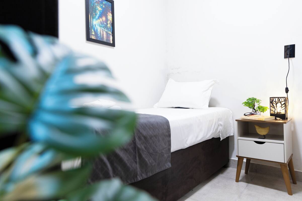 A bedroom with a bed, bedside table, and a potted plant.