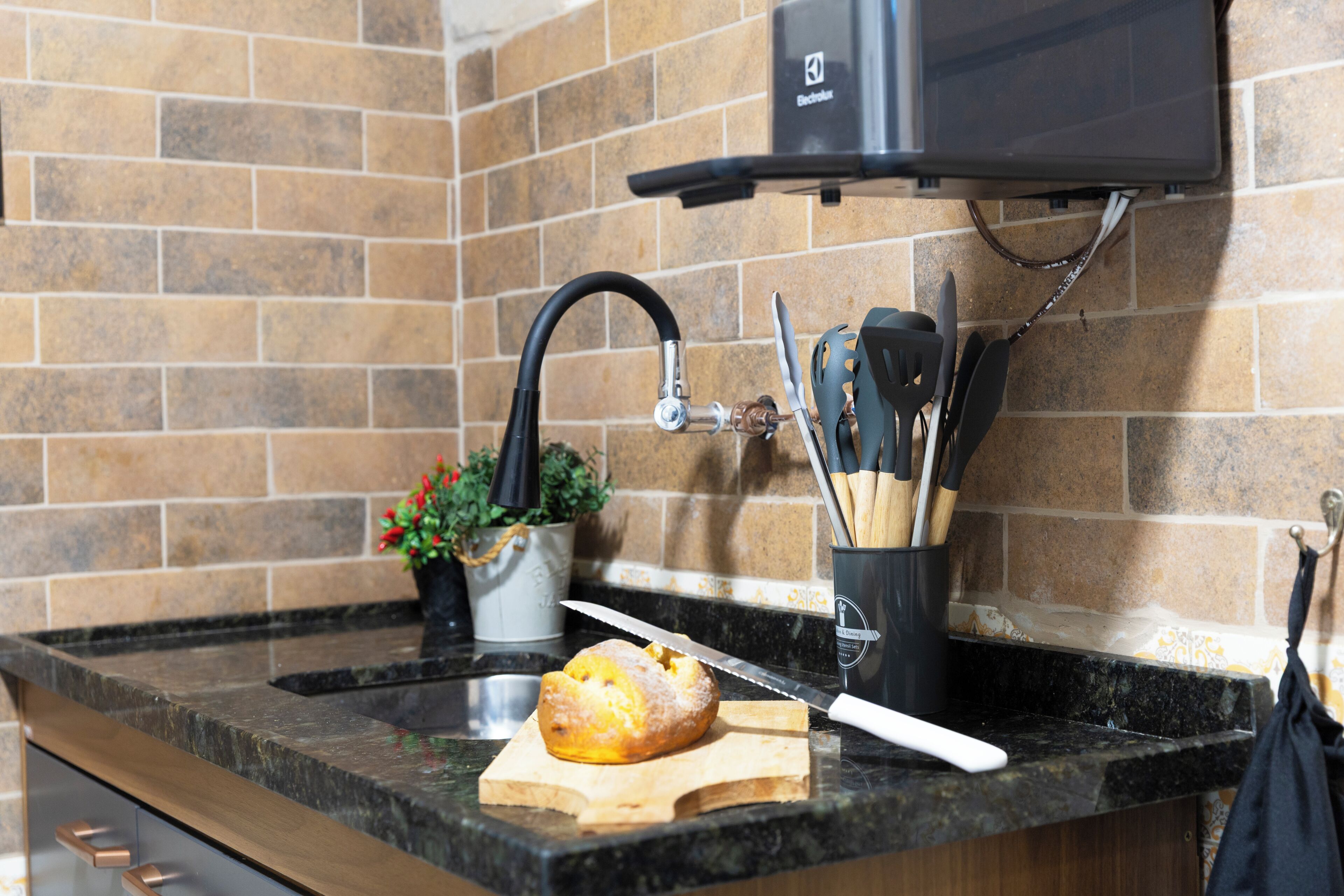 A kitchen with a granite countertop, a sink, a potted plant, and a knife on a cutting board.