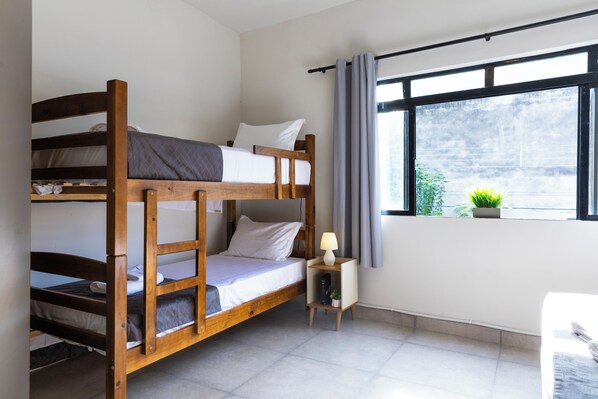 A bunk bed room with a small bedside table, a window with curtains, and a plant on the windowsill.