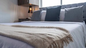 Ein ordentlich bezogenes Bett mit weißer Decke und beiger Tagesdecke.
