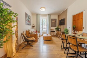A modern living room with a wooden floor, a sofa, a dining table with chairs, and a TV mounted on the wall. - Chez Aline Chic Central Chamonix 1BR w/ Brévent Views, Chamonix, France (Chamonix)