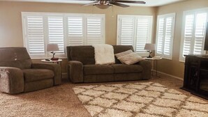 Un salon avec un canapé marron, un fauteuil marron, un tapis moelleux et un ventilateur de plafond.