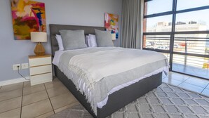 Ein modernes Schlafzimmer mit einem großen Bett, einem Nachttisch, einer Lampe und zwei abstrakten Bildern an der Wand.