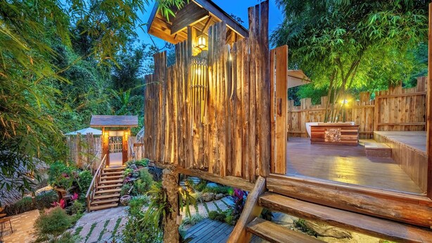Una terraza de madera con una escalera que conduce a un espacio cubierto, rodeada de abundante vegetación.