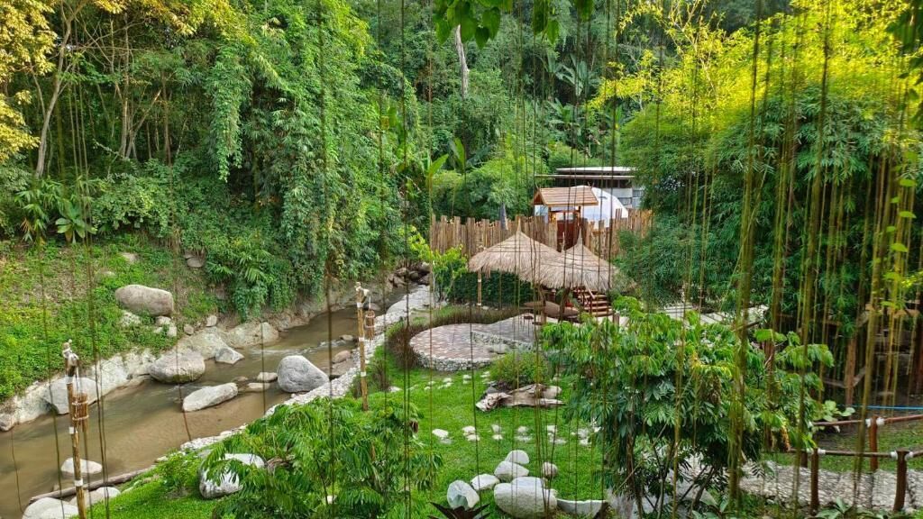A serene garden with a stream, rocks, and a thatched-roof structure.