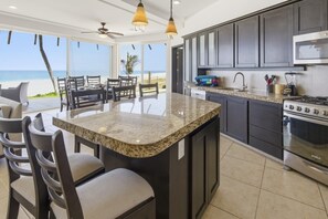 Una cocina con una isla grande, armarios oscuros y vistas a la playa.