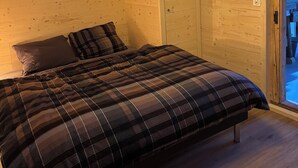 A bedroom with a wooden ceiling, a bed with a plaid duvet, and a door to the right. - Beautiful, gently renovated apartment in the beautiful Bernese Oberland. (Frutigen)