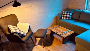 A cozy room with a wooden floor, a sofa, a chair, a small table, and a lamp. - Beautiful, gently renovated apartment in the beautiful Bernese Oberland. (Frutigen)